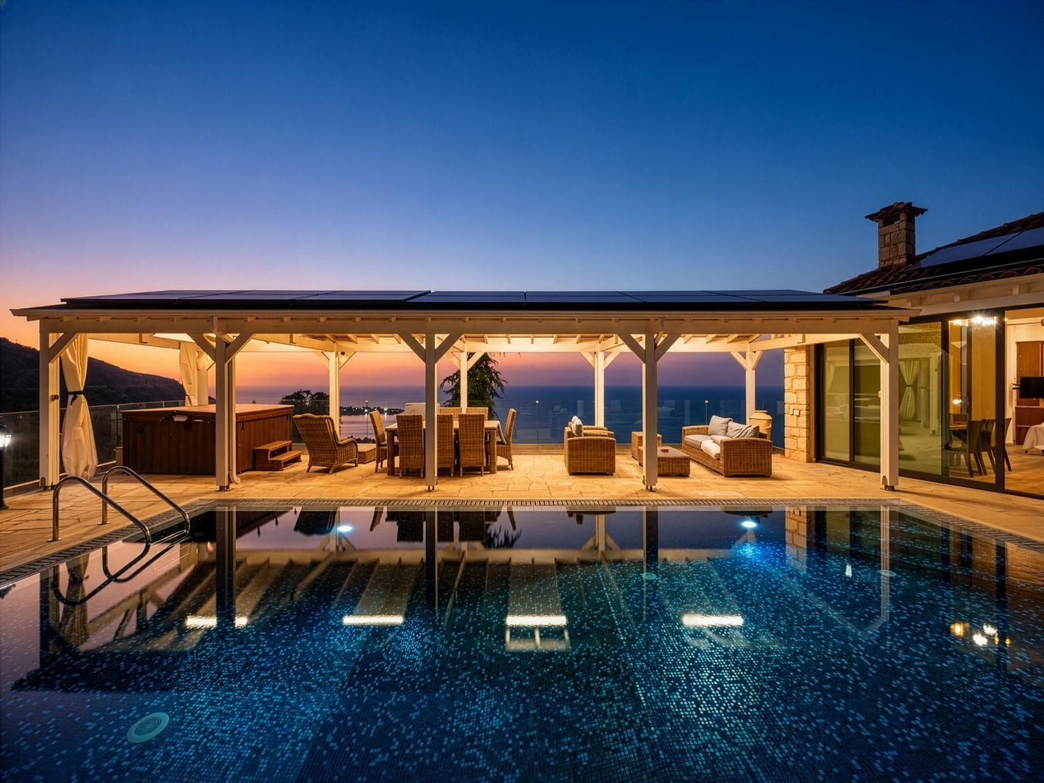 Una piscina infinita en la azotea con una zona de estar cubierta y vistas a la ciudad al atardecer.