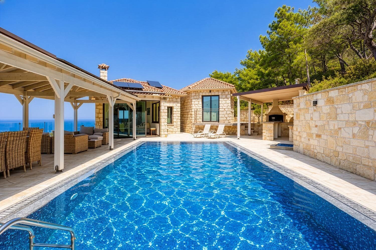 Une piscine agrémentée d’une pergola et de chaises longues, un bâtiment en pierre doté d’une cheminée, et une vue sur la mer.