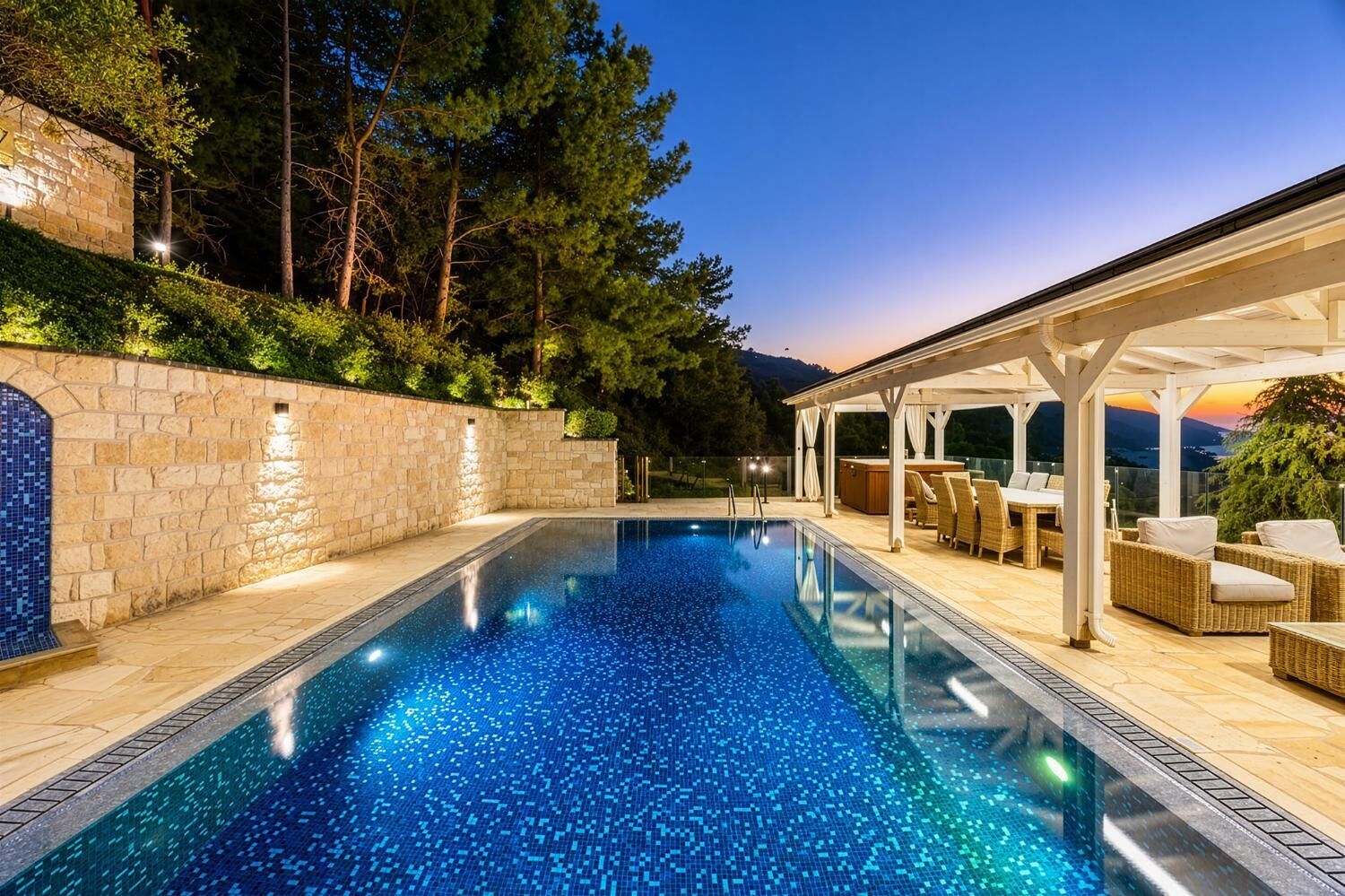 A swimming pool with a stone wall and a covered seating area with outdoor furniture.