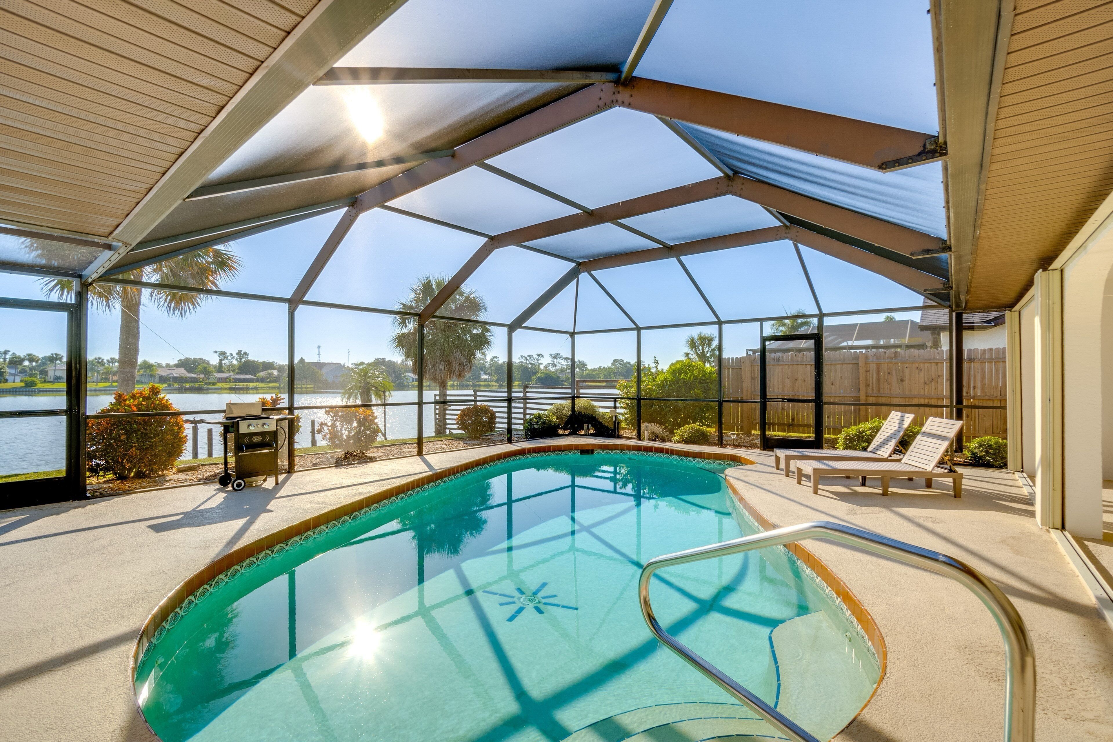 An indoor swimming pool with a glass enclosure, surrounded by lounge chairs and a view of a lake.