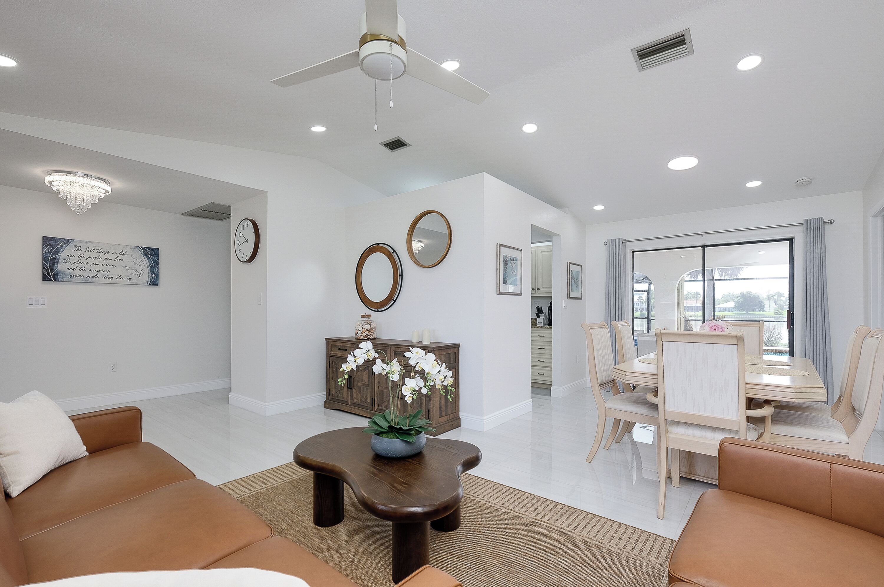A spacious living room with a ceiling fan, a dining area with a table and chairs, and a view through a large window.