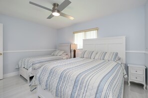 Ein Schlafzimmer mit zwei Betten, einem Deckenventilator, einem Nachttisch und einem Fenster mit Jalousien.