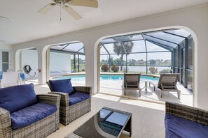 Eine sonnige Terrasse mit Korbmöbeln, einem Pool und Blick auf einen See.