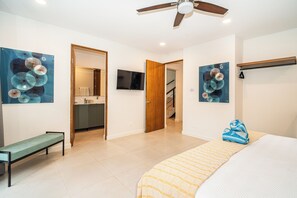 A hotel room with a bed, a bench, a ceiling fan, a TV, and artwork on the walls. - Villa LaLa Land • 13 Suites • 2 Pools • Party Room (Jaco)
