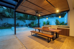 A covered outdoor patio with a wooden table and benches, surrounded by plants and a white wall. - Villa LaLa Land • 13 Suites • 2 Pools • Party Room (Jaco)