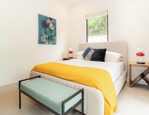 A modern bedroom with a bed, bedside tables, a bench, and a window. - Villa LaLa Land • 13 Suites • 2 Pools • Party Room (Jaco)