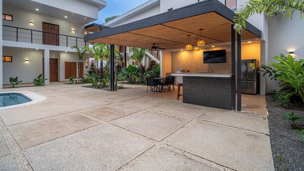 A modern outdoor kitchen area with a pool, surrounded by a spacious patio with a pergola. - Villa LaLa Land • 13 Suites • 2 Pools • Party Room (Jaco)