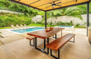 Eine Terrasse im Freien mit einem Holztisch und Bänken, einem Pool und einem Deckenventilator.