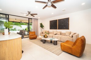 Ein modernes Wohnzimmer mit einer Couch, zwei Sesseln, einem Couchtisch und einem Deckenventilator.