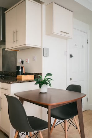 Uma cozinha compacta com armários brancos, cafeteira, planta e mesa de jantar com cadeiras.