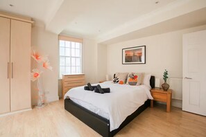 Quarto com cama, guarda-roupa, mesa de cabeceira, janela e um quadro na parede.