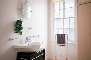 Ein modernes Badezimmer mit einem weißen Waschbecken, einem Spiegel und einem Fenster.