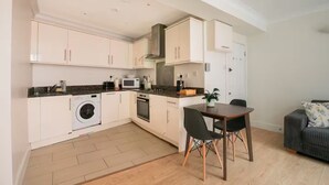 A compact kitchen with a dining area, a washing machine, a microwave, and a stove. - Cosy One-Double room flat near Big Ben (London)
