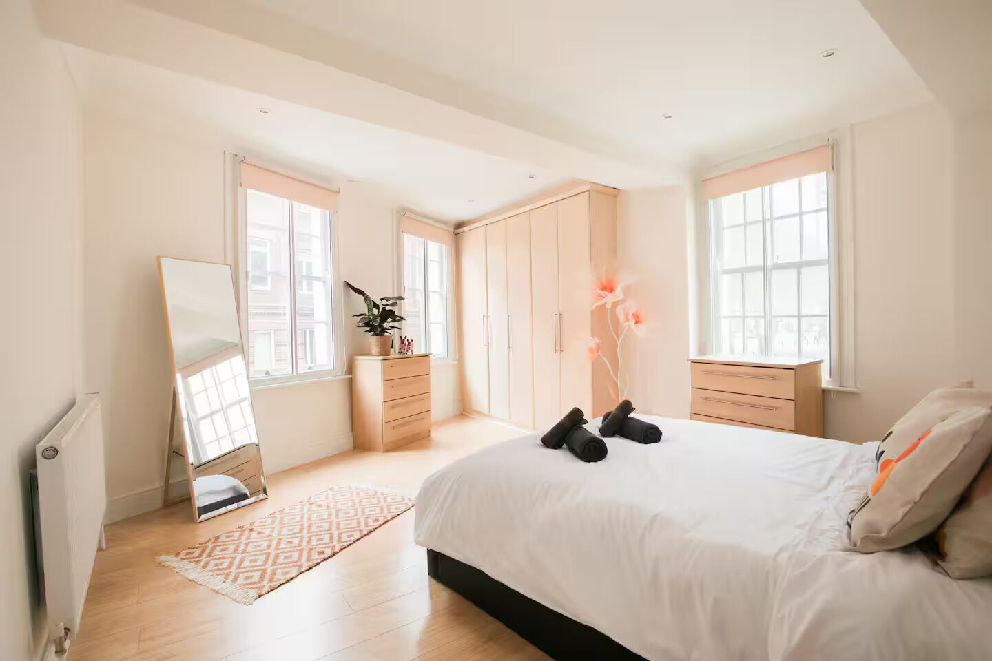Ein Schlafzimmer mit Bett, Kommode, Spiegel und Fenstern.