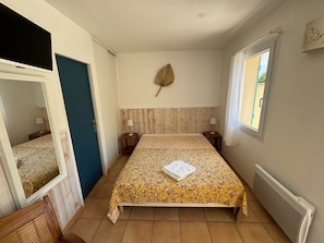 A bedroom with a bed, two bedside tables, a window, a radiator, and a mirror. - Jonquille Studio - Le Patio Residence (Mimizan)