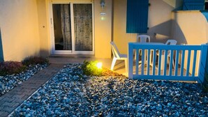 Een huis met pannendak, een schuifpui, een klein terras met een blauwe hek en een witte stoel.