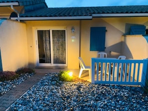 A house with a tiled roof, a sliding glass door, a small patio with a blue fence, and a white chair. - Jonquille Studio - Le Patio Residence (Mimizan)