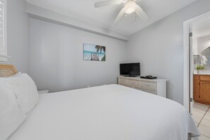 Une chambre à coucher avec un lit, un téléviseur posé sur une commode et un tableau accroché au mur.