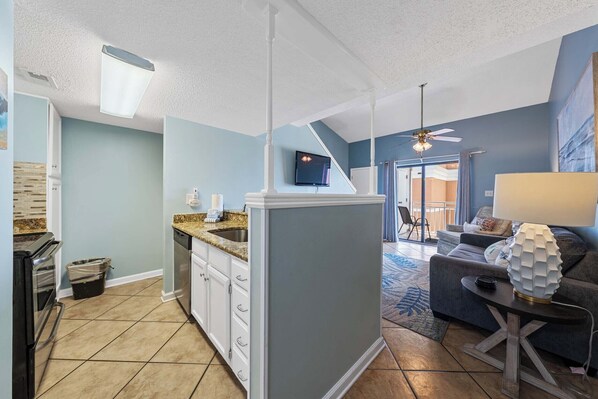 Eine moderne KĂŒche mit eingebautem GeschirrspĂŒler, ein Essbereich mit grauem Sofa und einem gemusterten Teppich sowie ein Deckenventilator.