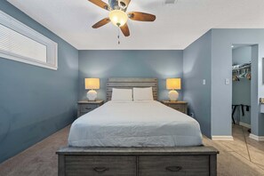 Une chambre à coucher comprenant un lit, deux lampes de chevet, un ventilateur de plafond et un dressing avec des vêtements suspendus.