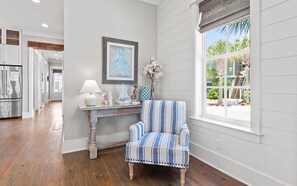A room with a striped armchair, a table with decorative items, and a window with a view of greenery. - 🏖️4 Bikes | Community Pool | 630 Steps to Beach | Pirate’s Smile🏖️ (Inlet Beach)