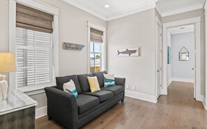 A living room with a dark grey sofa, a lamp, and a wall sign that reads 'DO NOT FEED THE SHARKS.' - 🏖️4 Bikes | Community Pool | 630 Steps to Beach | Pirate’s Smile🏖️ (Inlet Beach)