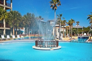 Ein Pool mit einer zentralen Fontäne, umgeben von Liegestühlen und Palmen.