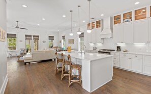 A modern kitchen with white cabinetry, a large island with bar stools, and a dining area with a sofa and table. - 🏖️4 Bikes | Community Pool | 630 Steps to Beach | Pirate’s Smile🏖️ (Inlet Beach)