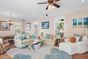 A spacious living room with a high ceiling, a ceiling fan, and a large window with blinds. There are multiple pieces of furniture including a sofa, a coffee table, and a chair. - 🏖️ The Mermaid | Private Pool • 6 Bikes • Walk to Beach 🌊 (Inlet Beach)