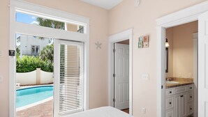 Ein Schlafzimmer mit einem großen Fenster, einer Tür zu einem Badezimmer und Blick auf ein Schwimmbecken.