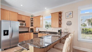 Eine moderne Küche mit Holzschränken, einem Edelstahl-Kühlschrank, einer Granitarbeitsplatte und Blick ins Freie durch große Fenster.