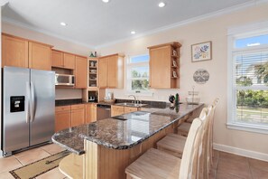 A modern kitchen with wooden cabinets, a stainless steel refrigerator, a granite countertop, and a view of the outdoors through large windows. - 🏖️ The Mermaid | Private Pool • 6 Bikes • Walk to Beach 🌊 (Inlet Beach)