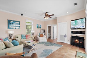 Ein helles Wohnzimmer mit Kamin, Fernseher und Deckenventilator.