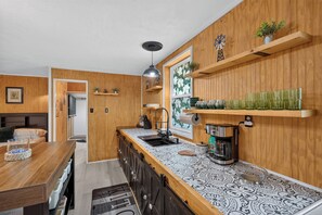 A kitchen with wooden paneling, a built-in oven, a coffee maker, and a window with a floral view. - Brand new Cozy 1-bedroom building in charming Lake Placid with AC (Lake Placid)