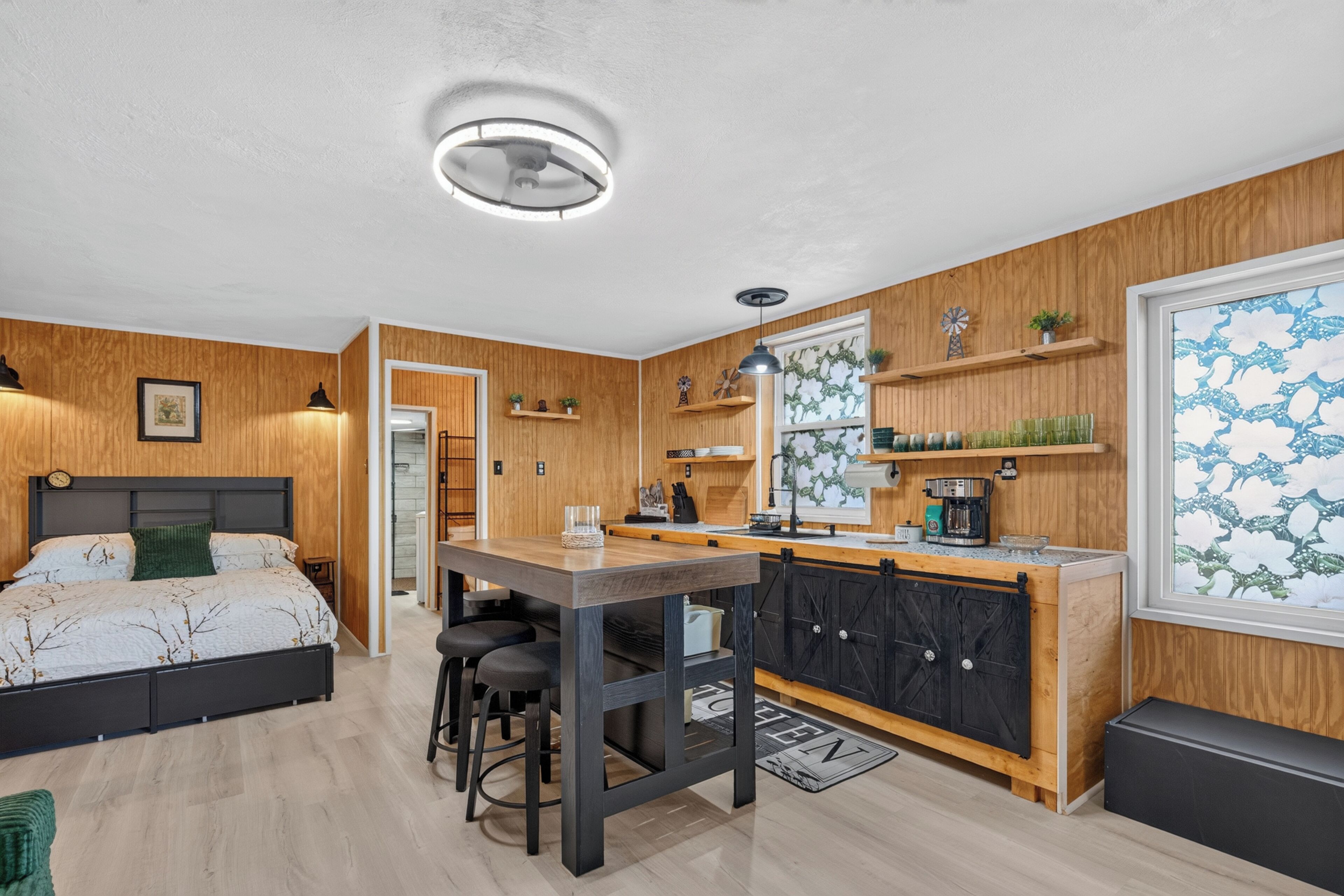 A modern bedroom with a bed, a desk, and a kitchenette.