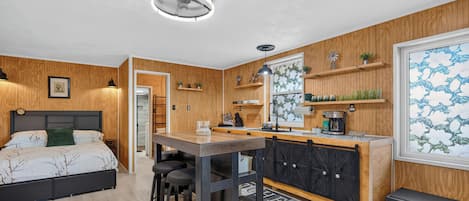 A modern bedroom with a bed, a desk, and a kitchenette.