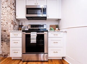 A kitchen with white cabinets, a stainless steel oven, and a microwave. - Midnight Inn, Garden B - Ground-Floor Historic Luxury on Monterey Square (Savannah)