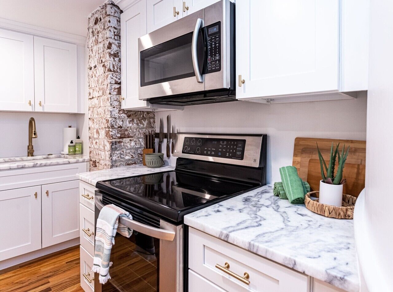 A kitchen with white cabinets, a stainless steel microwave, a black stove, and a marble countertop.