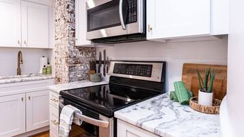 A kitchen with white cabinets, a stainless steel microwave, a black stove, and a marble countertop.