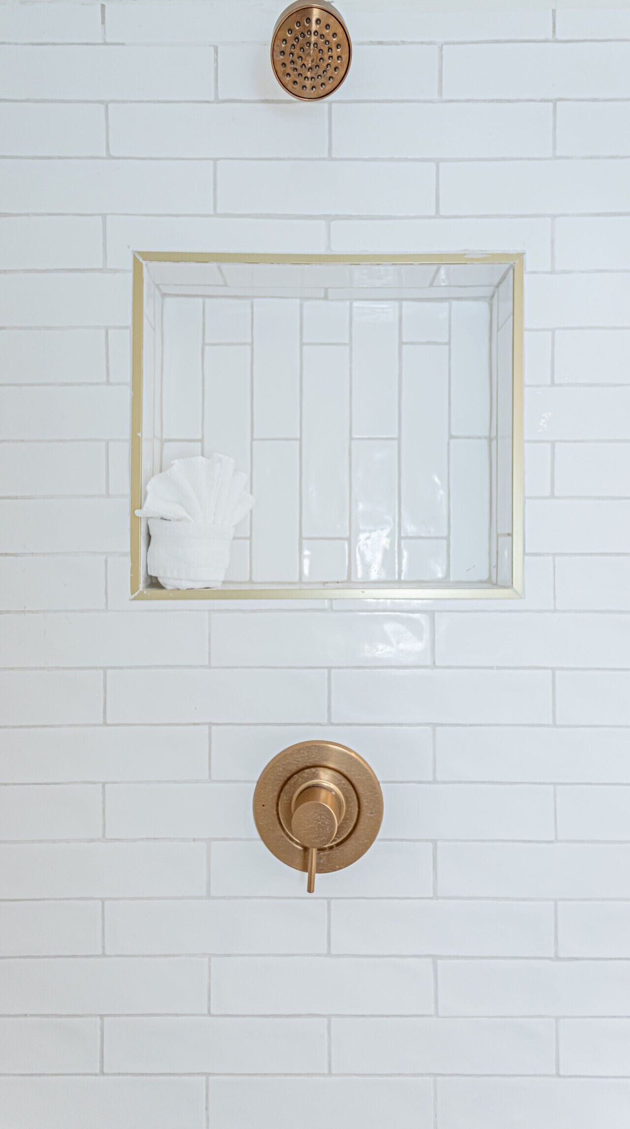 A bathroom with a white tiled wall, a rectangular mirror with a gold frame, and a gold faucet.