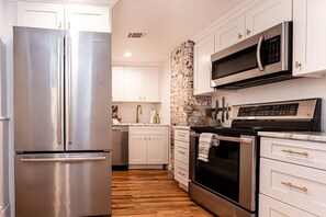 Cocina moderna con electrodomésticos de acero inoxidable, muebles de cocina blancos, una pared de acento de piedra y suelo de madera.