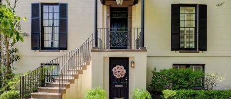 A two-story building with a black front door, a small porch with a railing, and a staircase leading to the entrance.
