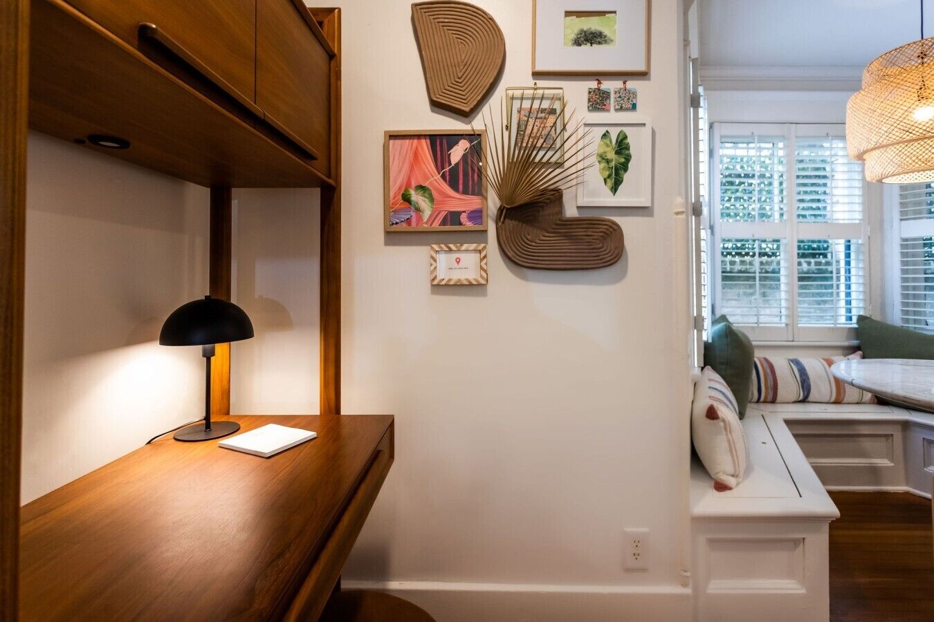 A room with a wooden desk, a black lamp, and a wall with framed artwork and a decorative plant.
