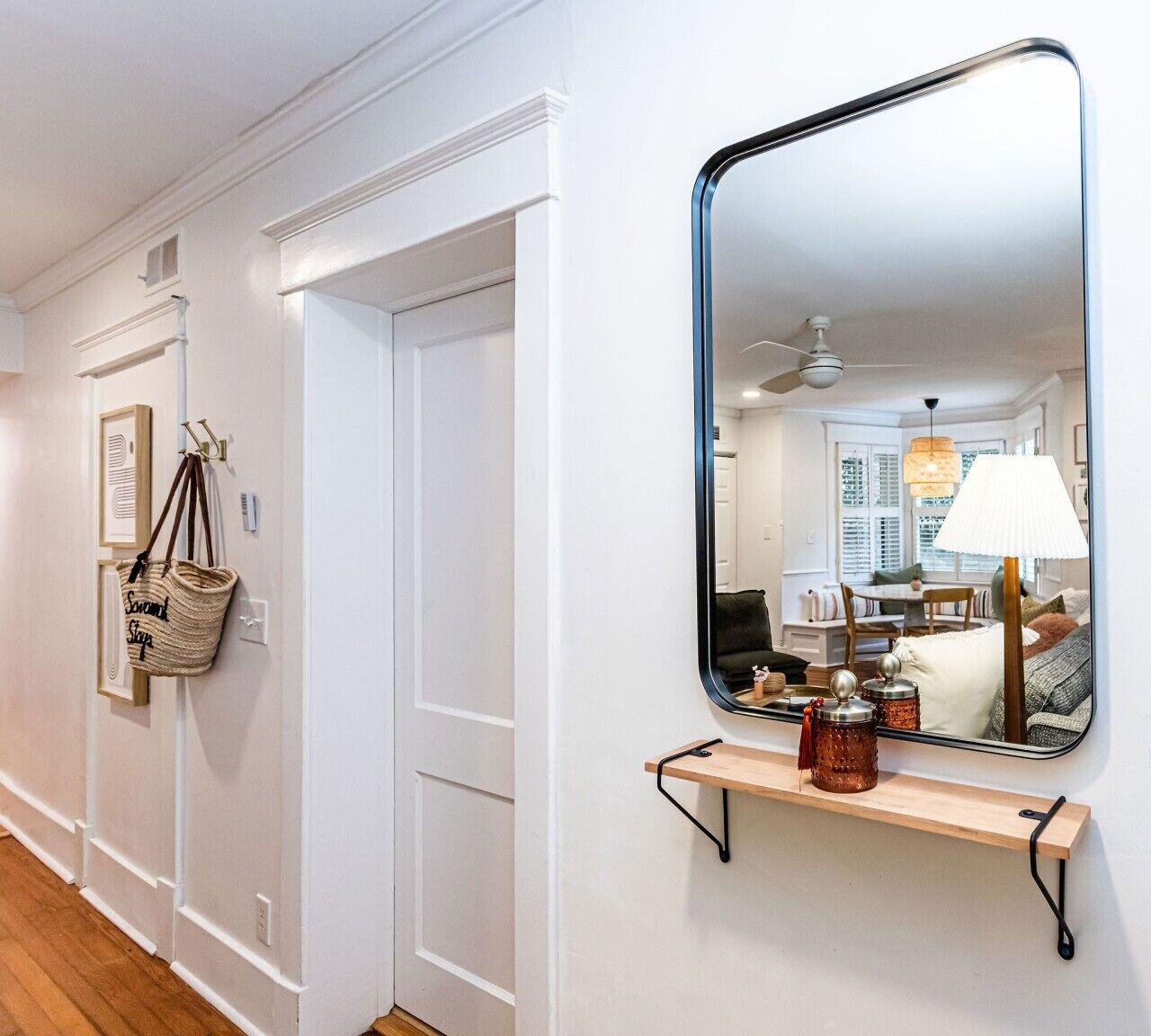 A hallway with a white door, a mirror, and a wooden shelf with jars.