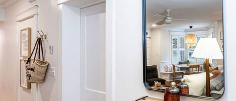 A hallway with a white door, a mirror, and a wooden shelf with jars.