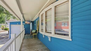 Varanda coberta com piso de madeira, grade branca e parede externa azul.