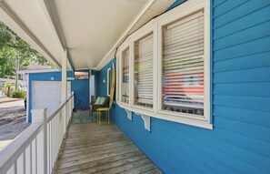 Ein überdachter Balkon mit Holzboden, weißem Geländer und einer blauen Außenwand.
