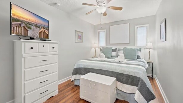 Um quarto com uma cama, cômoda, ventilador de teto, televisão e janela.
