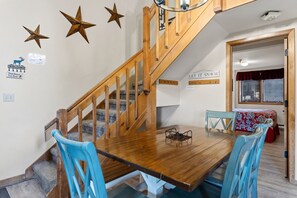 Un coin repas avec une table en bois et des chaises bleues, un escalier avec des rampes en bois et des éléments décoratifs en forme d’étoiles sur le mur.