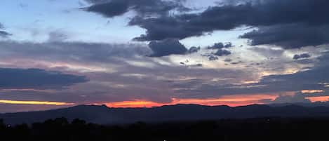 A sunset over a mountainous landscape with a road and streetlights in the foreground.